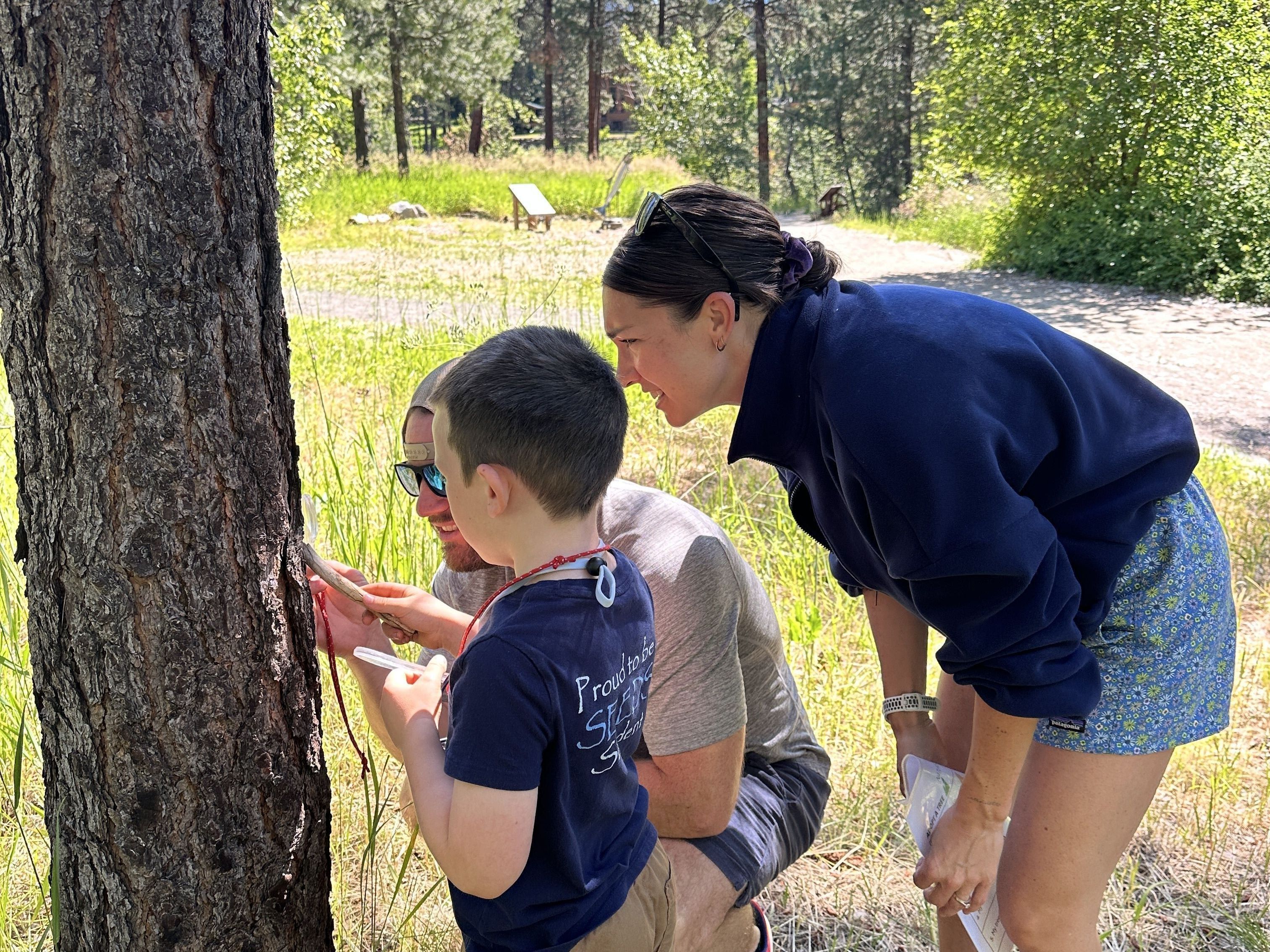 Two adults helping a student with inspecting a tree during a Field Day.