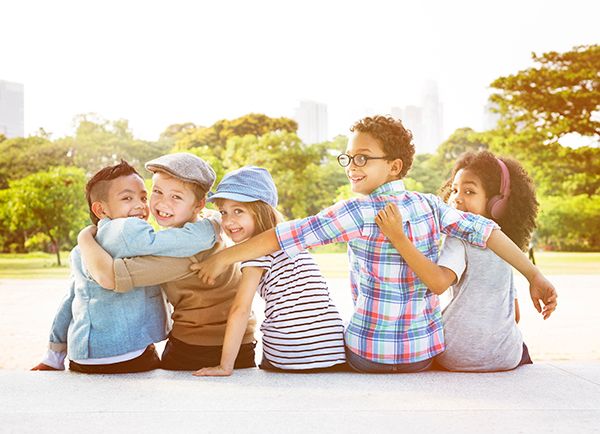 5 children sitting together, looking back with their arms on each other's shoulders