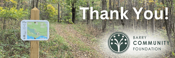 A trail map with a trail extending into a forest with leaves on the ground.