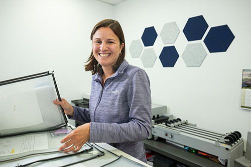 Lauren Mumley standing at counter holding plastic sleeves containing print job tickets