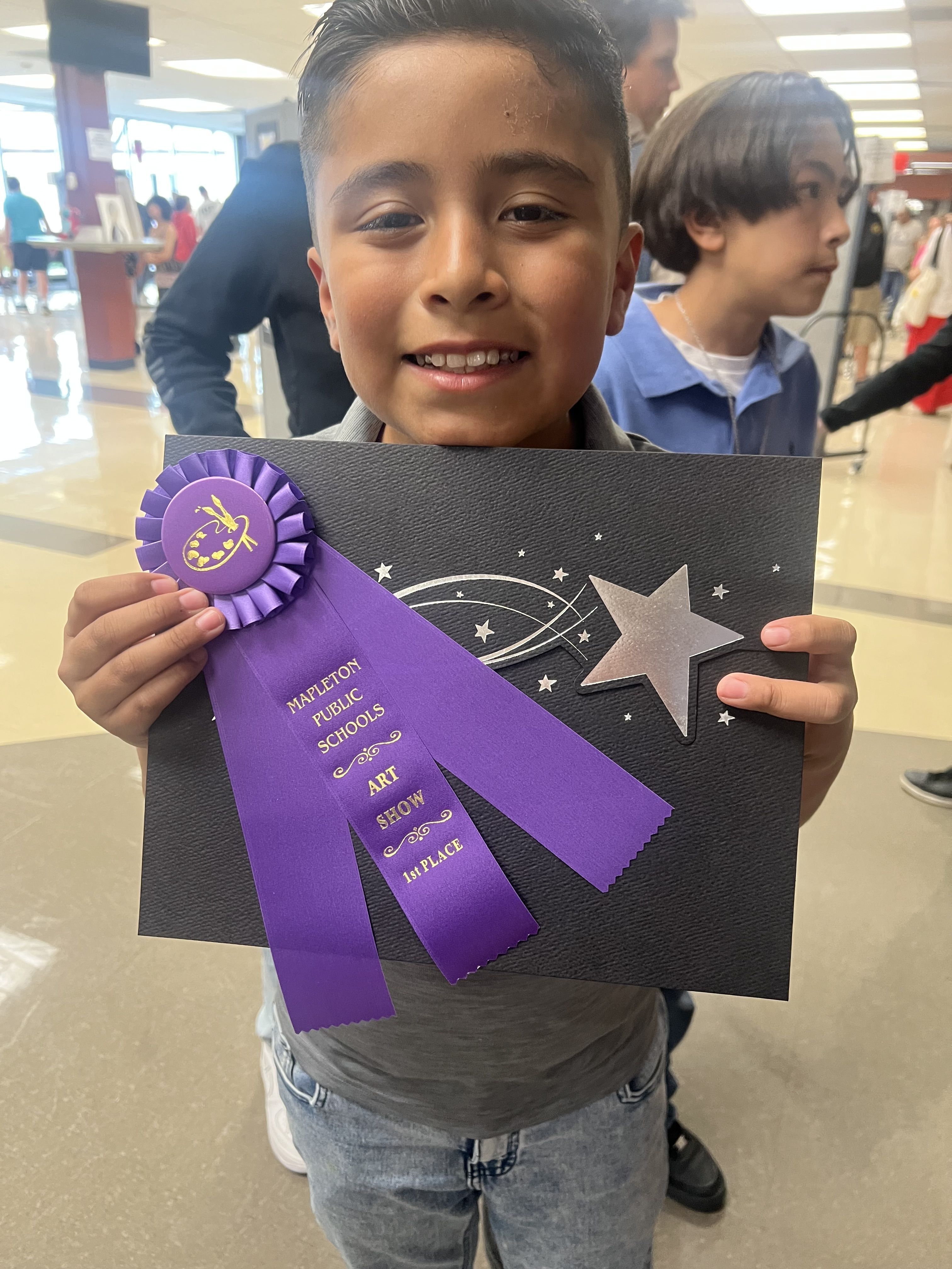 Mapleton student proudly holds artwork with a ribbon award at the District Art Show