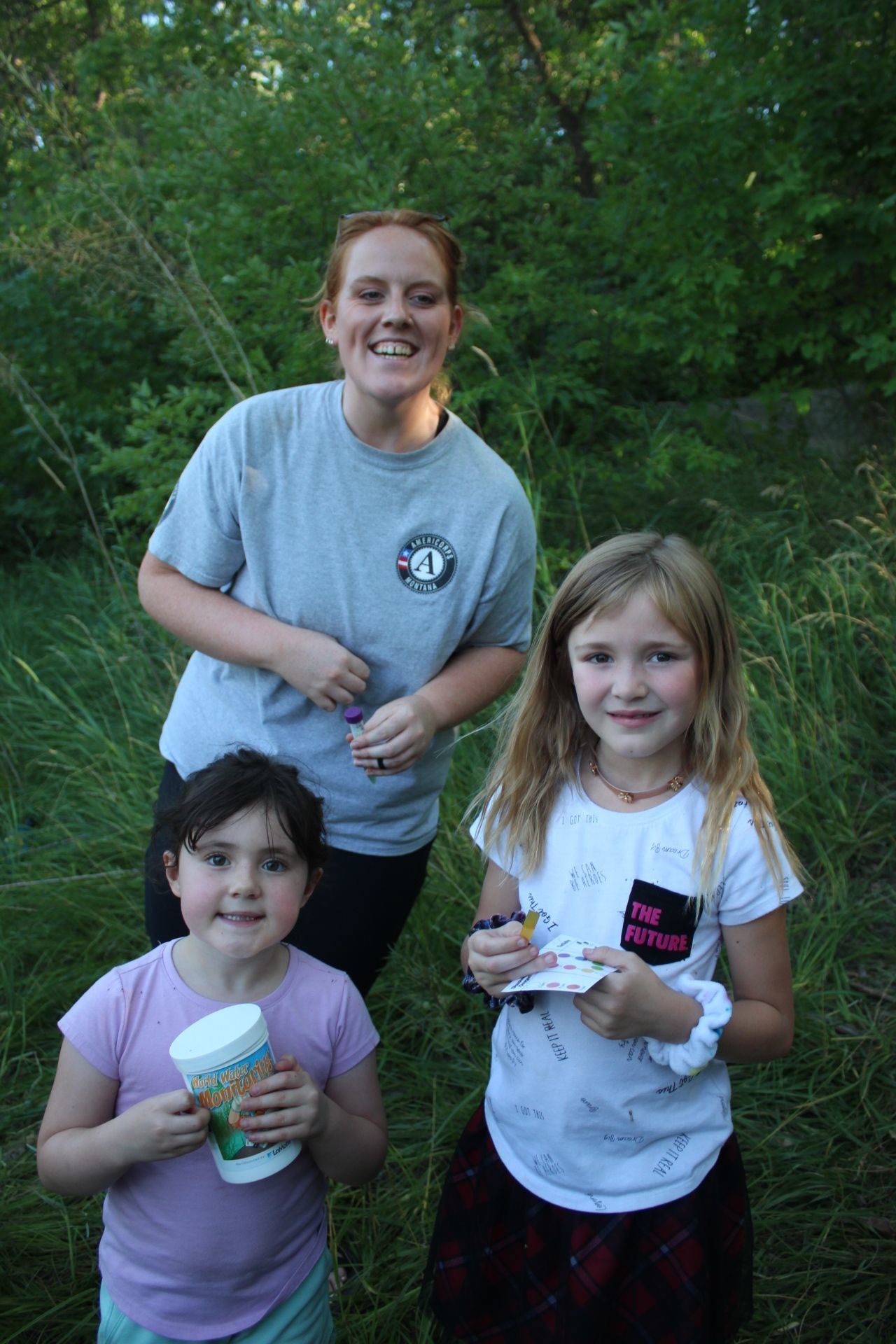 Maggie poses with two children at a water stewardship outreach event.