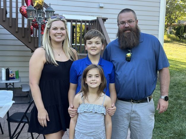 L-R: Katie stands with her son, daughter, and husband outside a house.