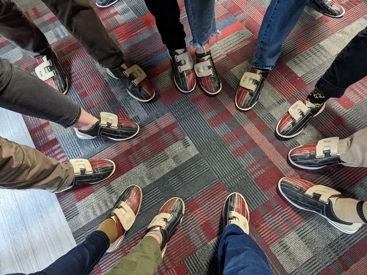  [Image Description: A circle of people's feet, wearing bowling shoes. This was taken at an MCC bowling event.]
