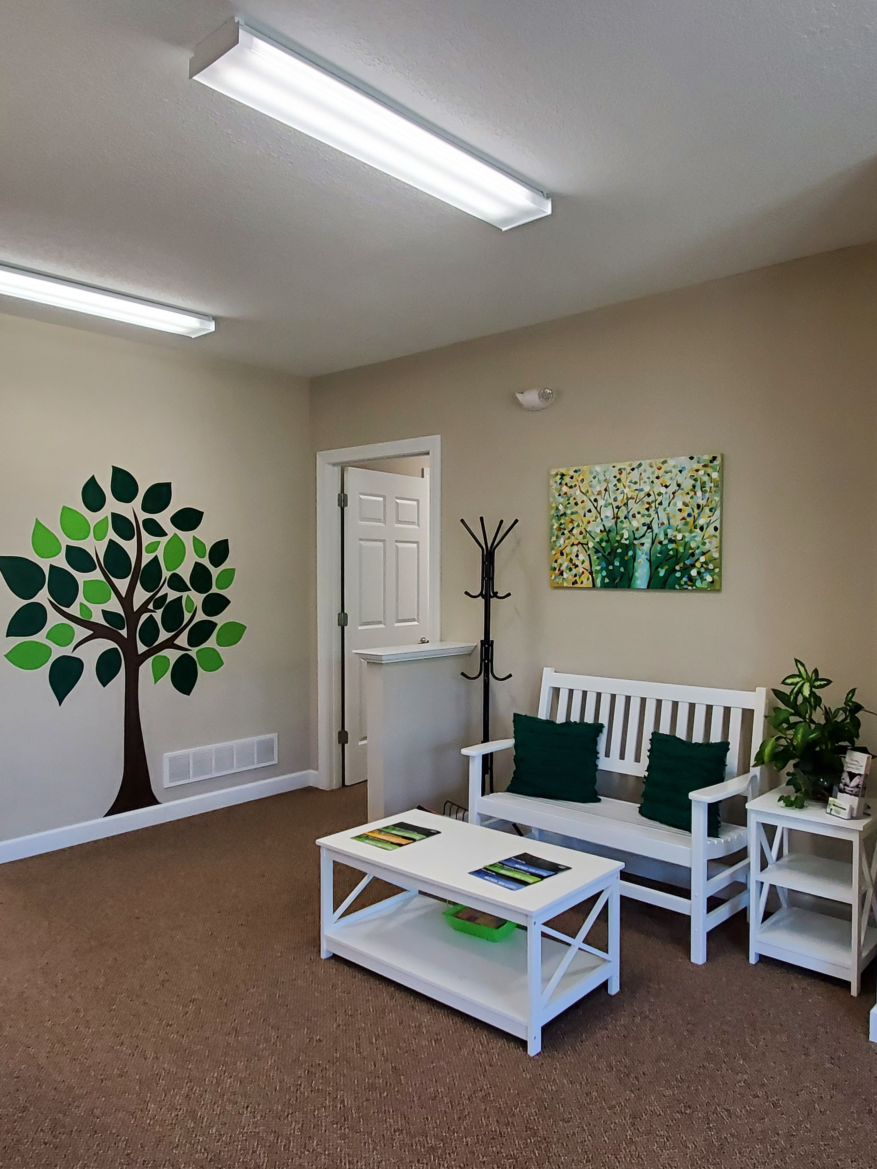 Photo of the lobby of Lifeline's clinic. Including a mural of a tree, and a family friendly waiting room with benches and pillows.