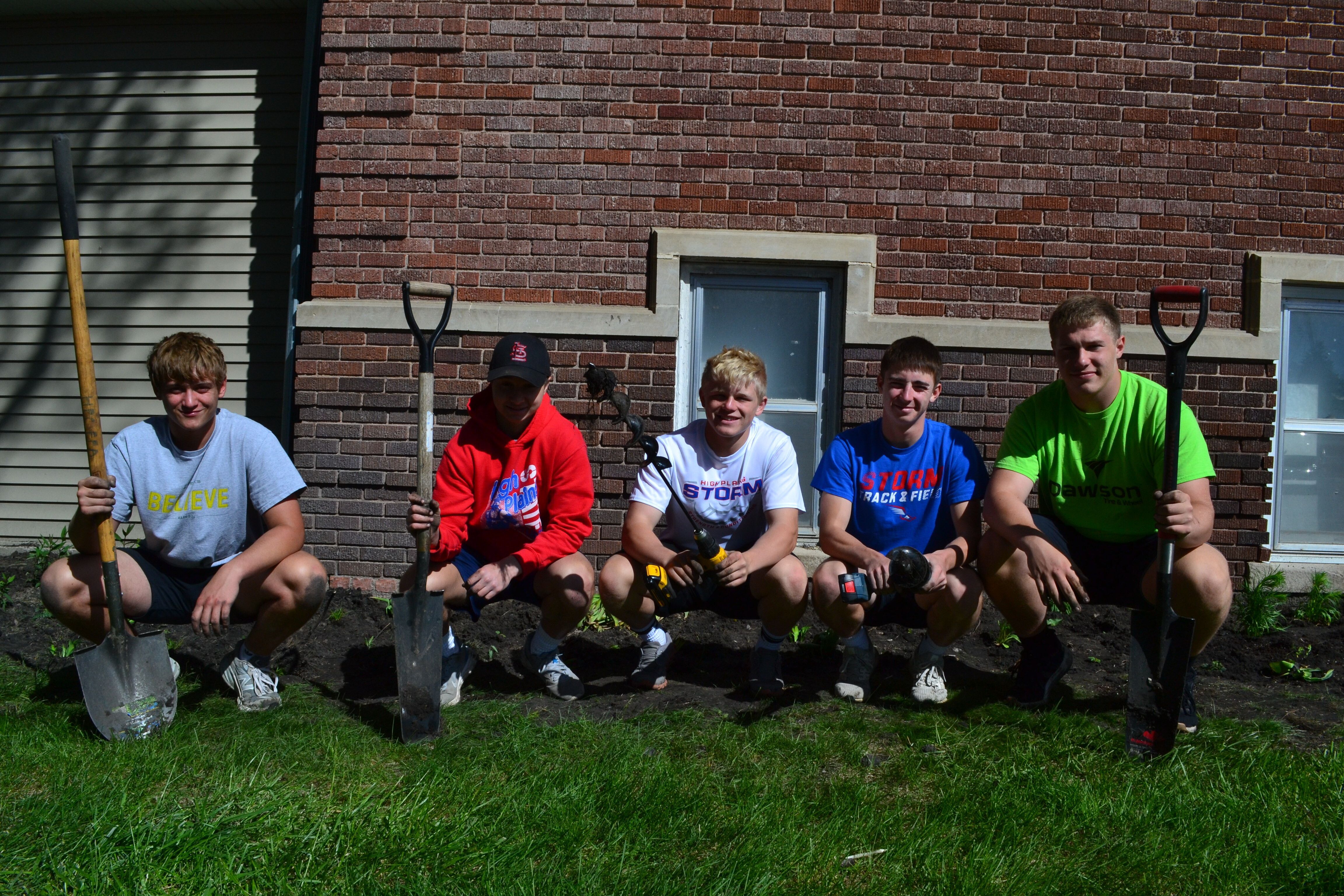 A group of high school boys pose with gardening tools in front of a newly dug garden bed 