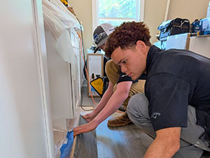 Volunteer applying caulk along baseboard trim