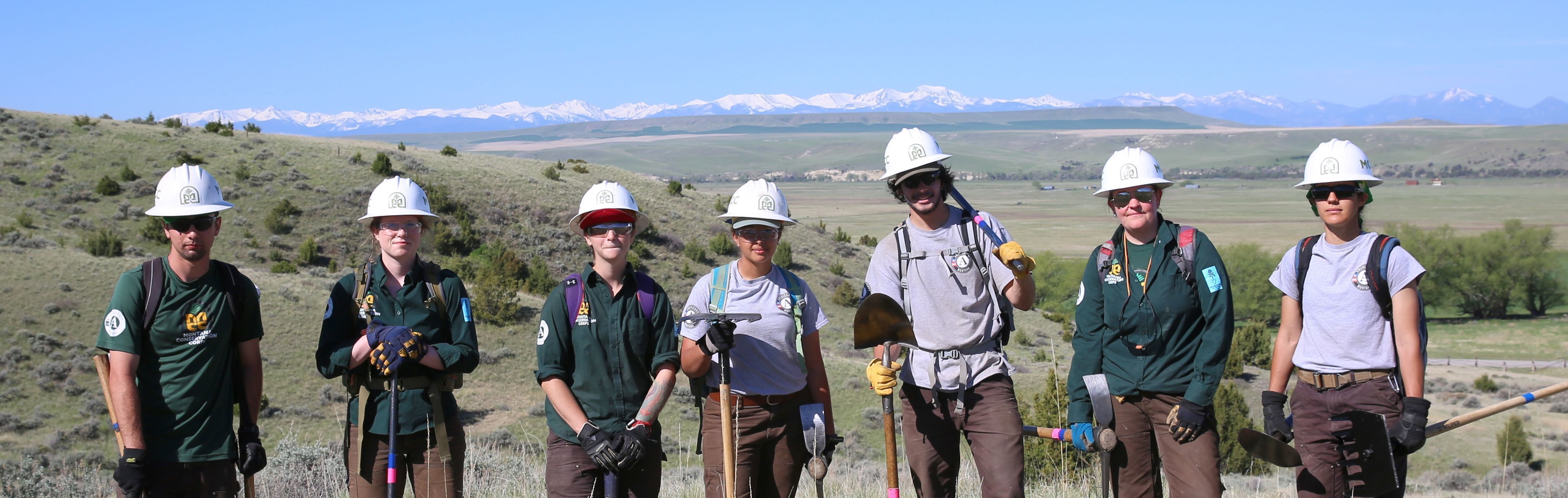 [Image description: Seven MCC members standing together. In the background, the rolling sagebrush covered hills are seen, along with purple peaks.]