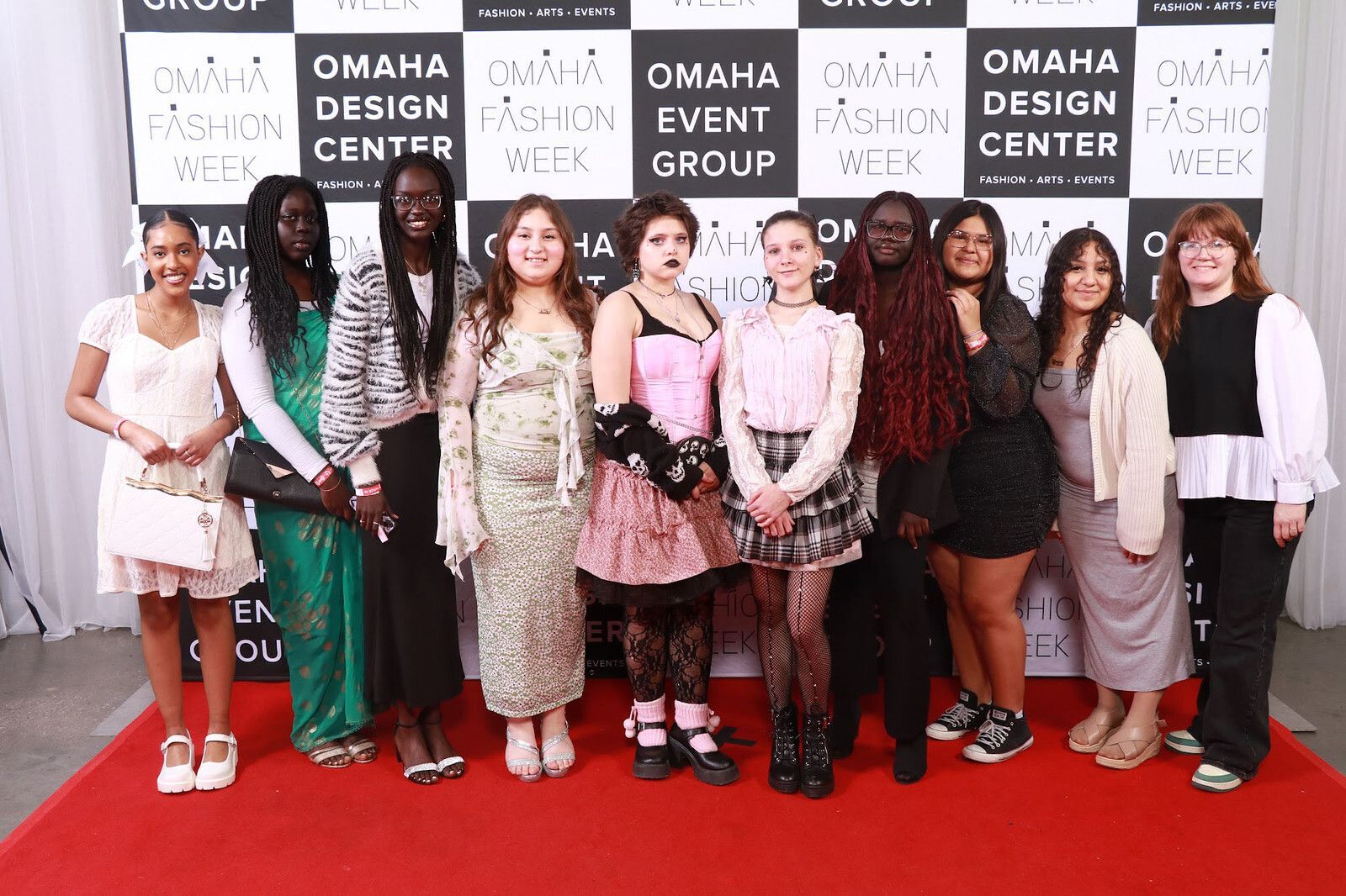 A group of 10 students standing on a red carpet in front of an "Omaha Fashion Week" backdrop 