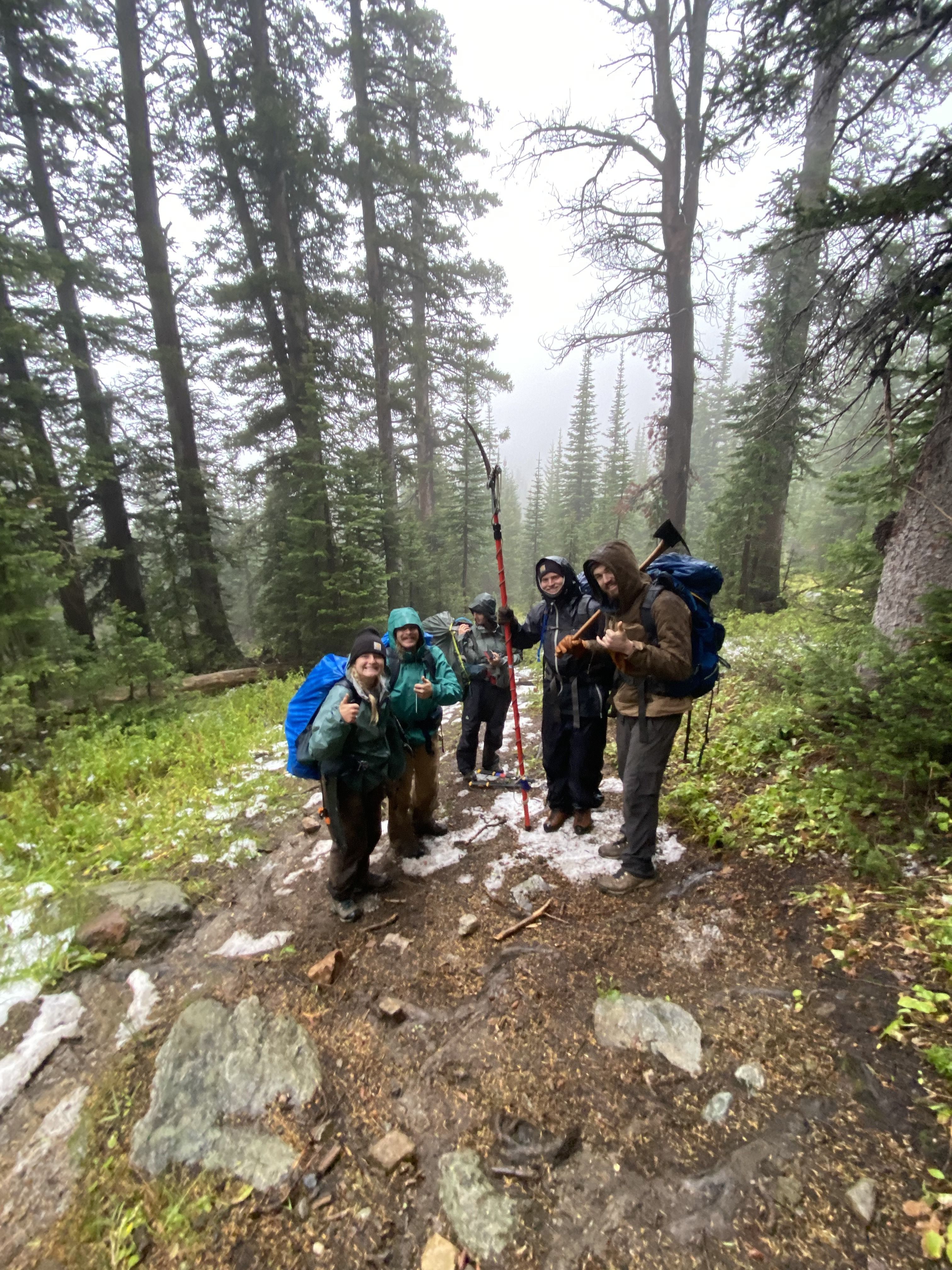 A crew stands decked out in rain gear, smiling and carrying tools.