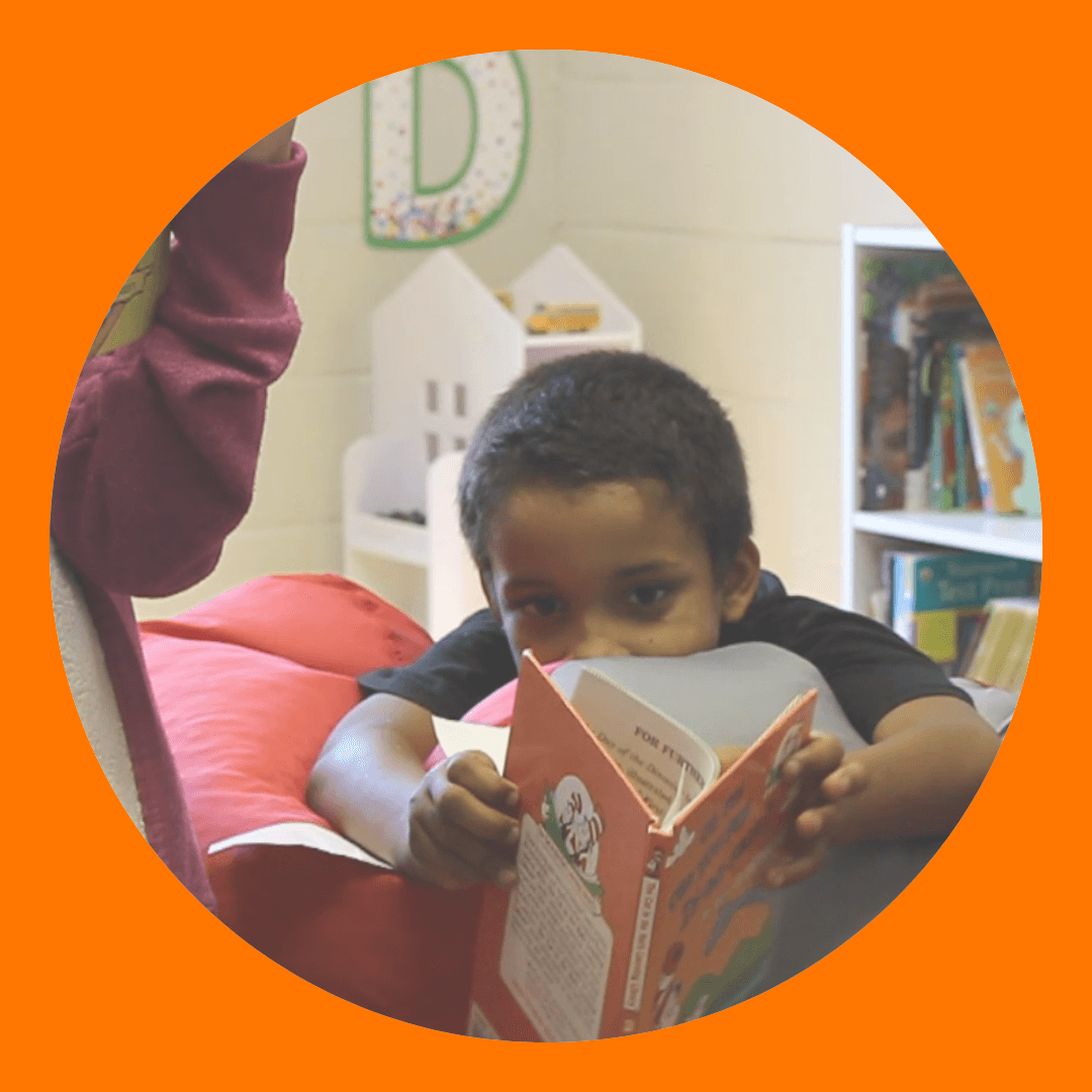 Circular image with orange border of a child reading a book while laying on a bean bag chair