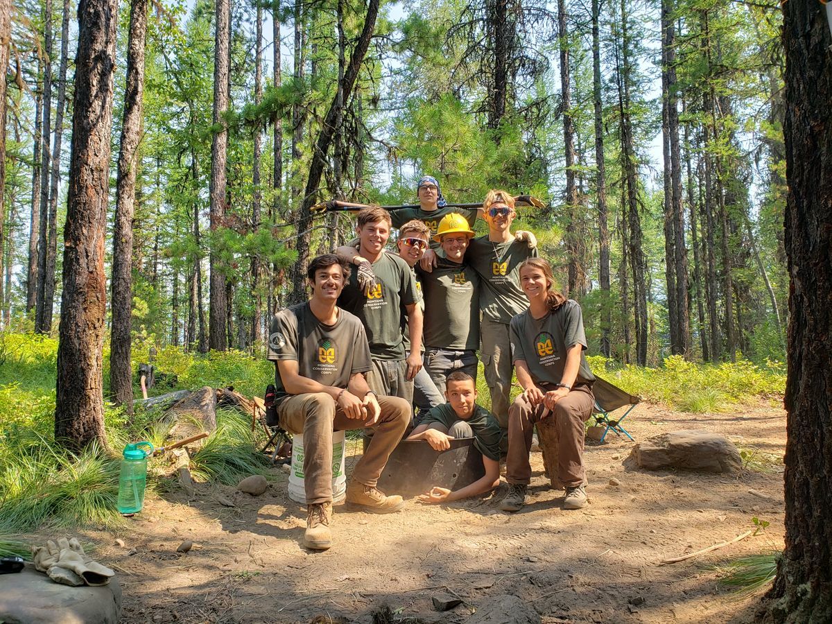 [Image Description: Eight MCC members along with their Leader sit in a freshly maintained campsite, all looking at the camera and smiling. A forest is behind them.] 