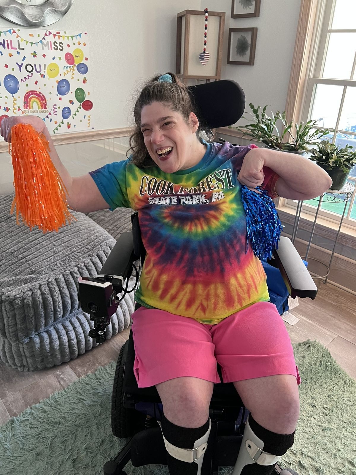 A woman in a wheelchair smiles waving orange and blue pom poms