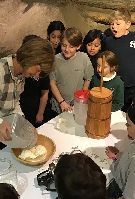 Woman in plaid shirt showing group of children how to make butter.
