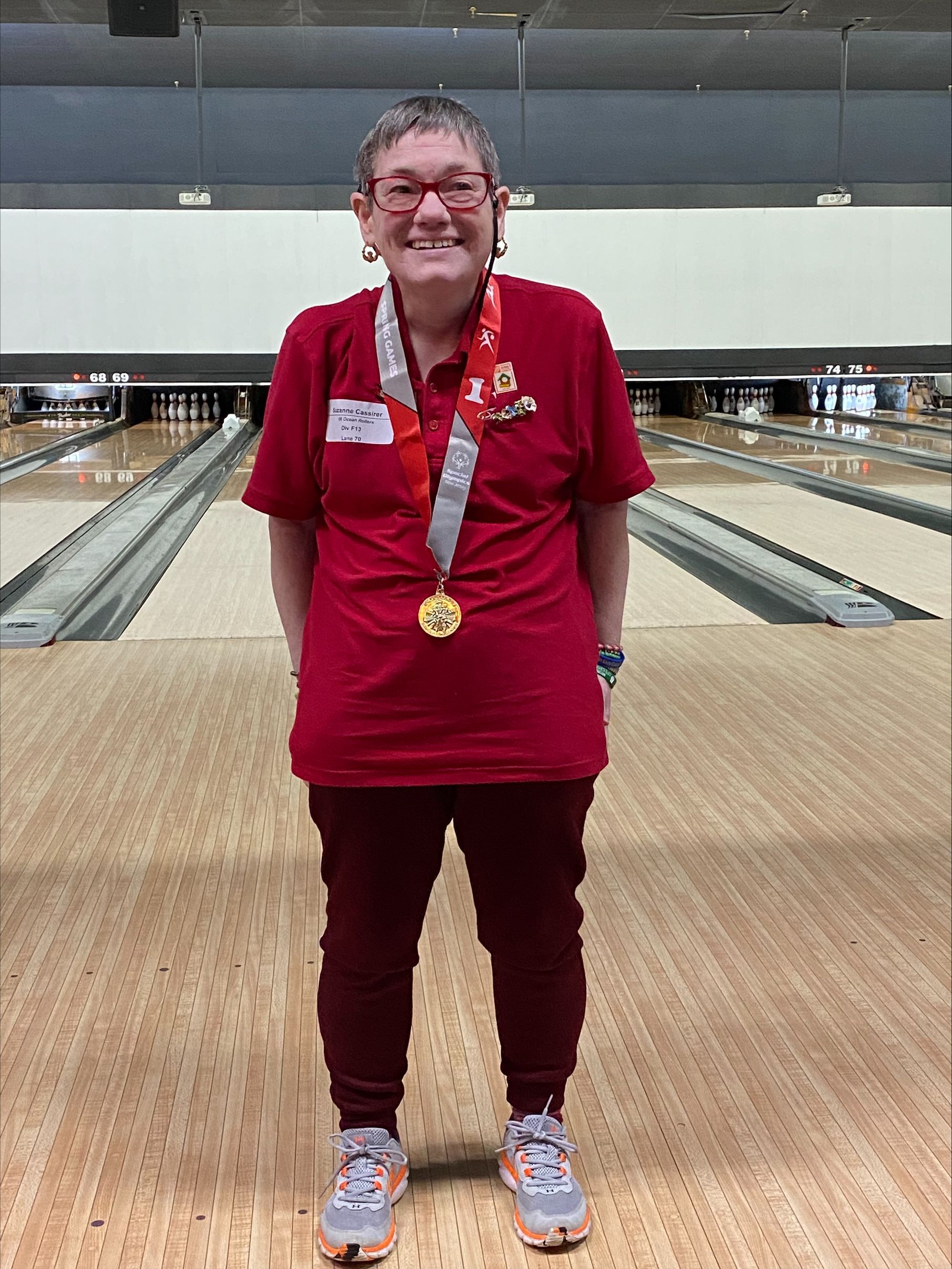 A smiling woman wearing a red shirt and gold medal.