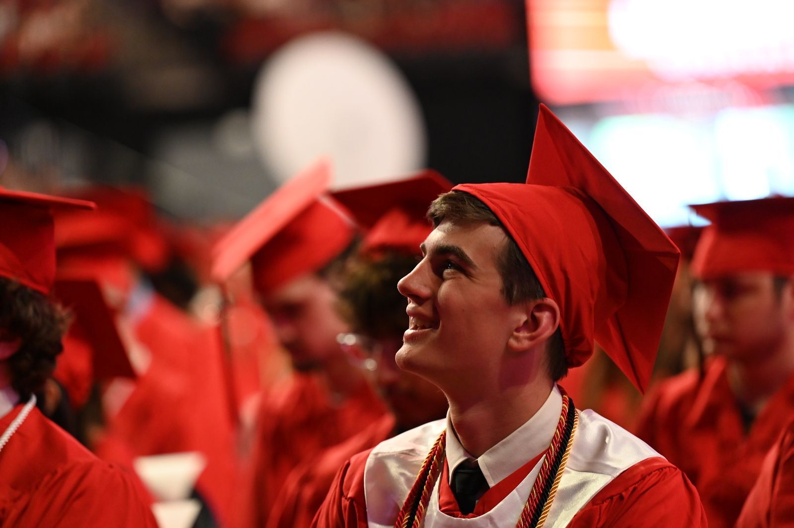 student in red cap and gown sitting and smiling at graduation ceremony
