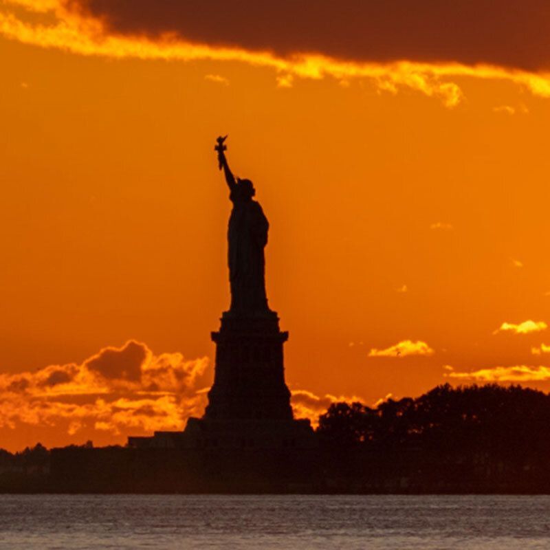 Silhouette of the Statue of Liberty against an orange sunset sky.