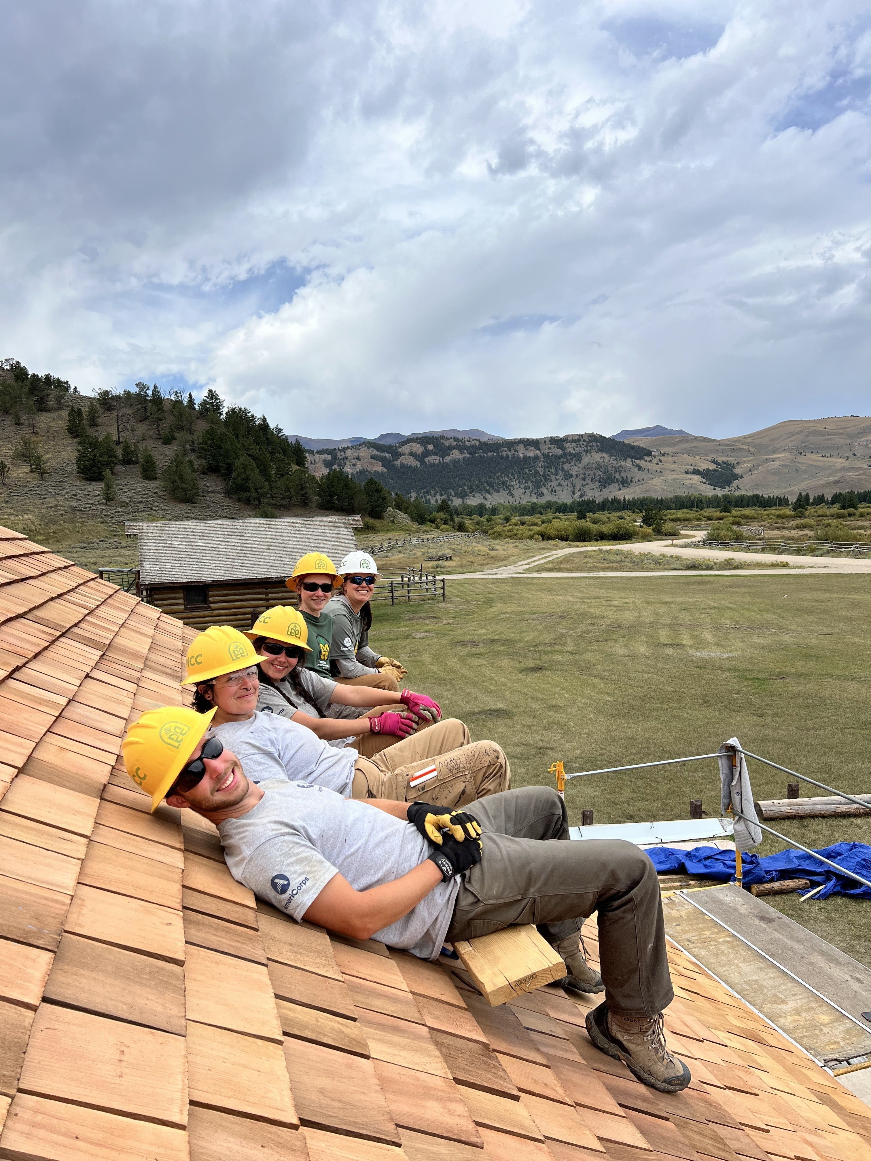 A crew sits on a freshly replaced roof, smiling at the camera.