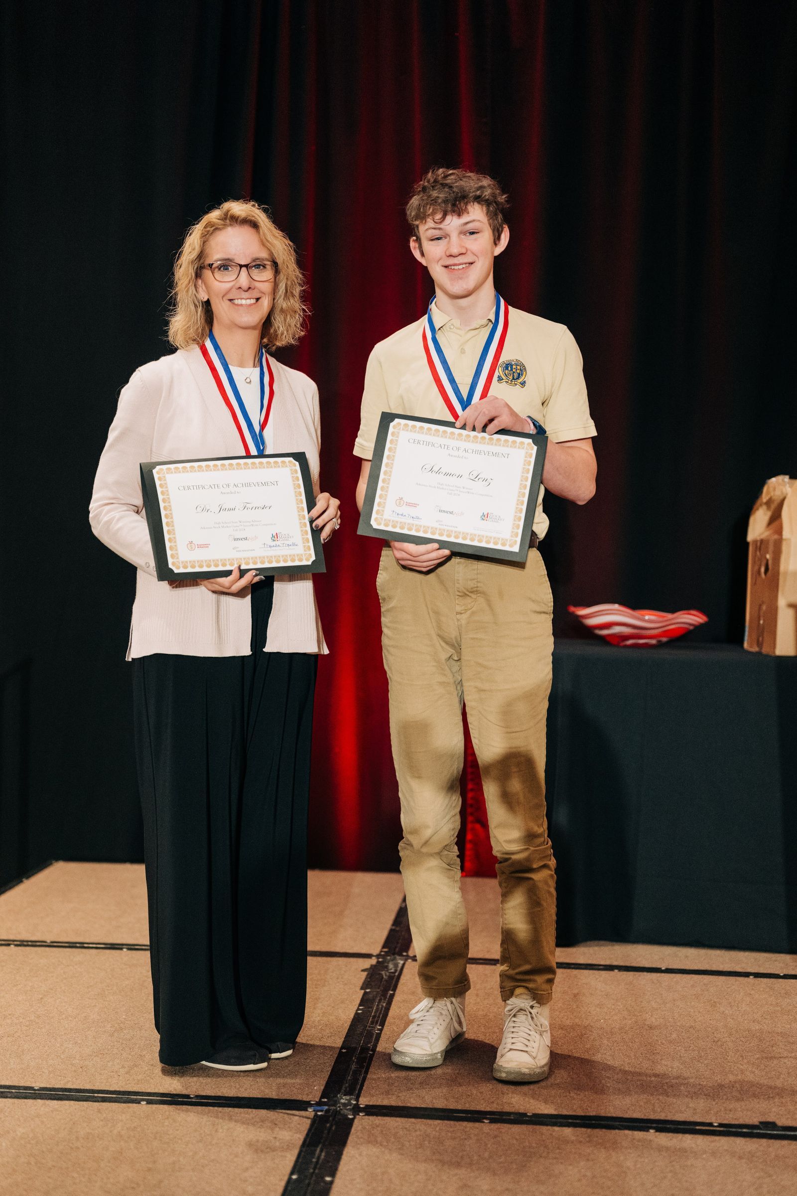 young boy holding certificate standing next female teacher holding certificate