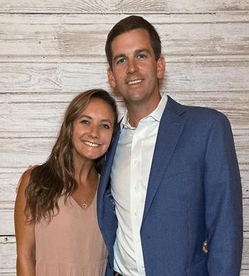 A tall young man has his arm wrapped around a shorter woman, and they are both smiling.