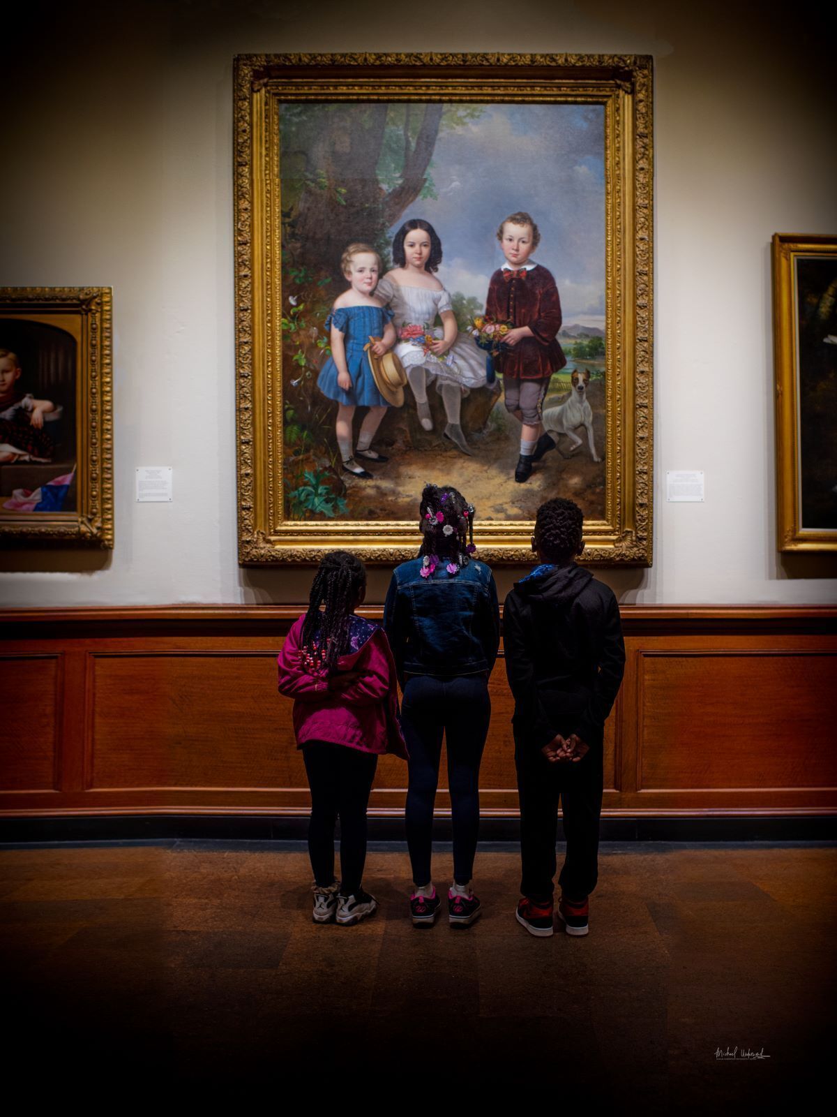 three children looking at a painting in a museum gallery