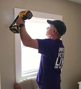 Purple Heart Homes volunteer using a drill to install window trim indoors