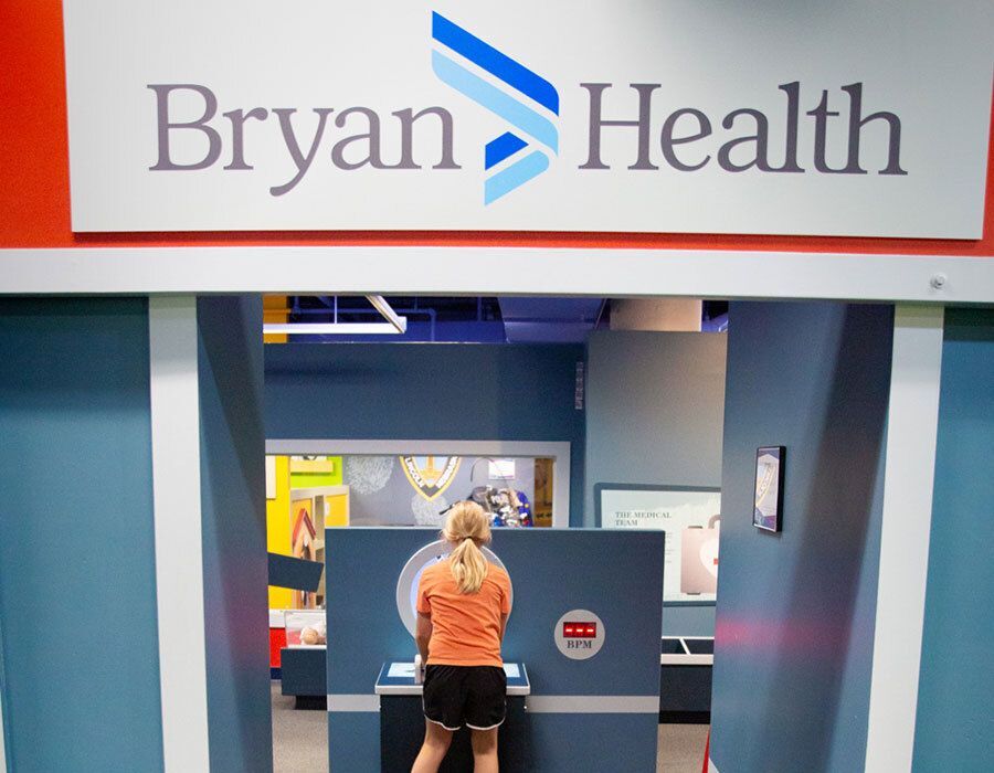 A child interacts with an exhibit under a "Bryan Health" sign in a museum-like setting.