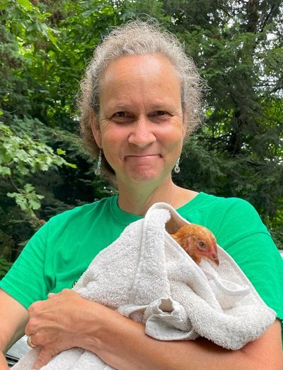 An older woman smiles as she holds a chicken wrapped in a bath towel.