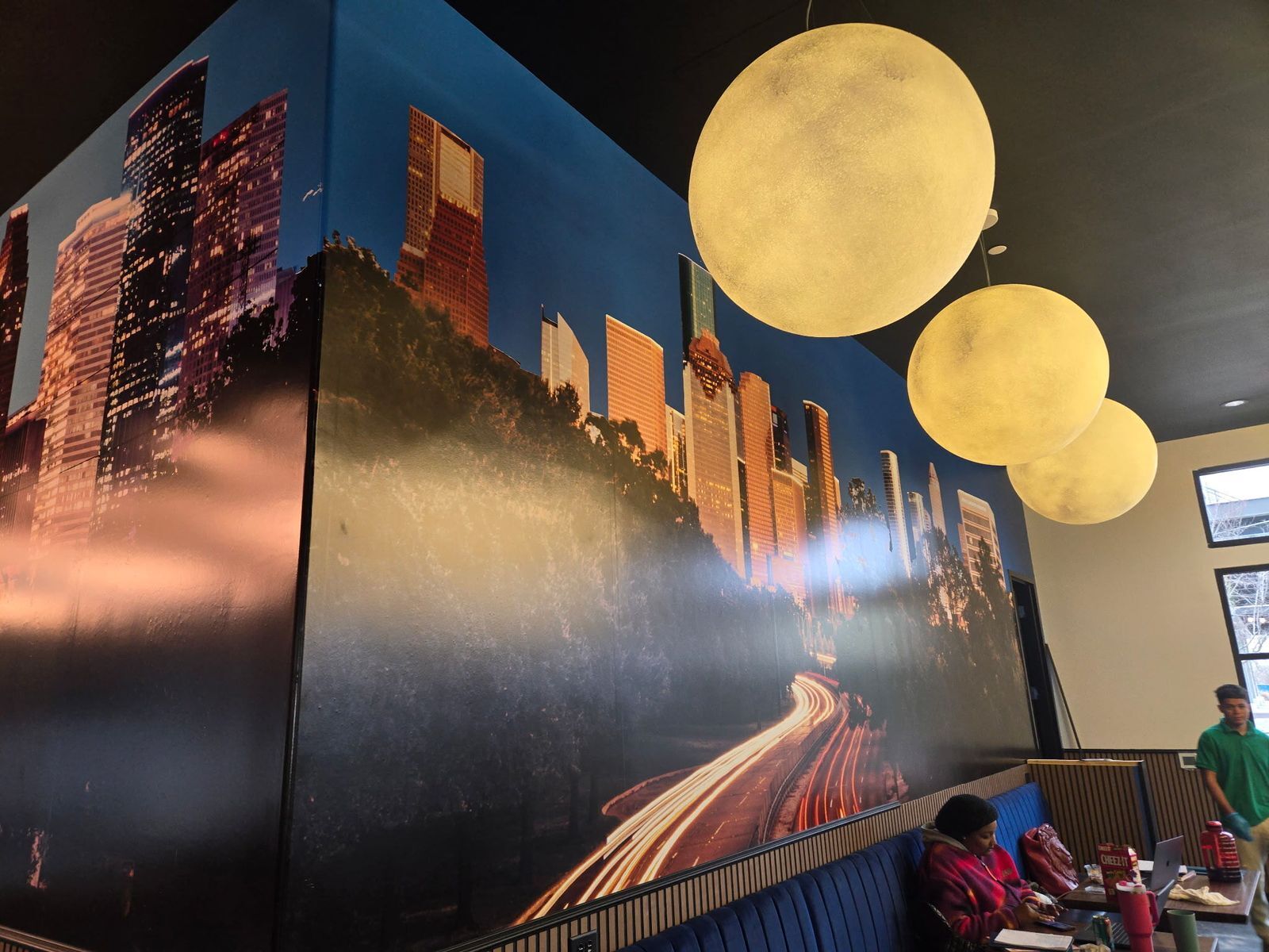  Large-scale custom wall wrap displaying a high-resolution image of the Houston skyline at night with illuminated buildings and light trails, wrapping around a corner inside a modern dining space.