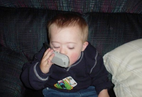 Toddler boy with Down syndrome holds cell phone up to ear to talk.