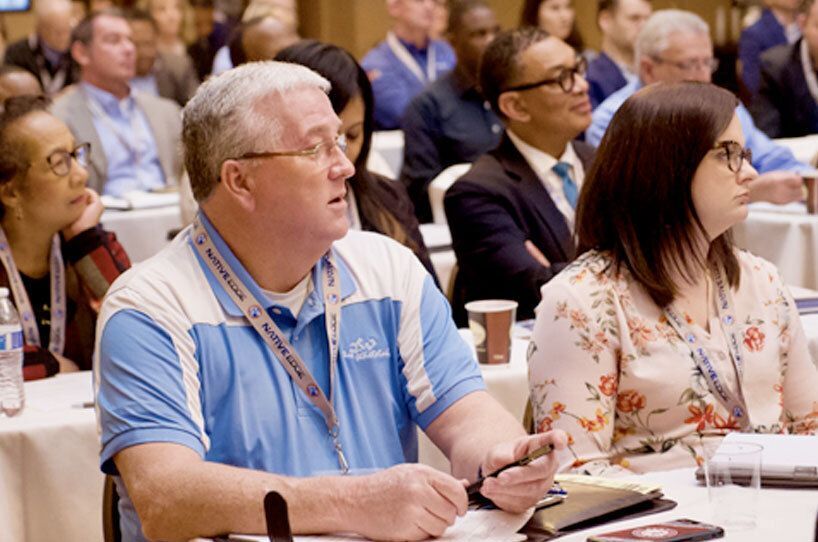 People seated at a conference, listening attentively.