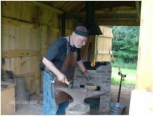 Person working at an anvil in a wooden blacksmith's workshop.
