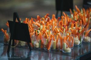 Several cups with dressing and long carrot sticks sit on a table.