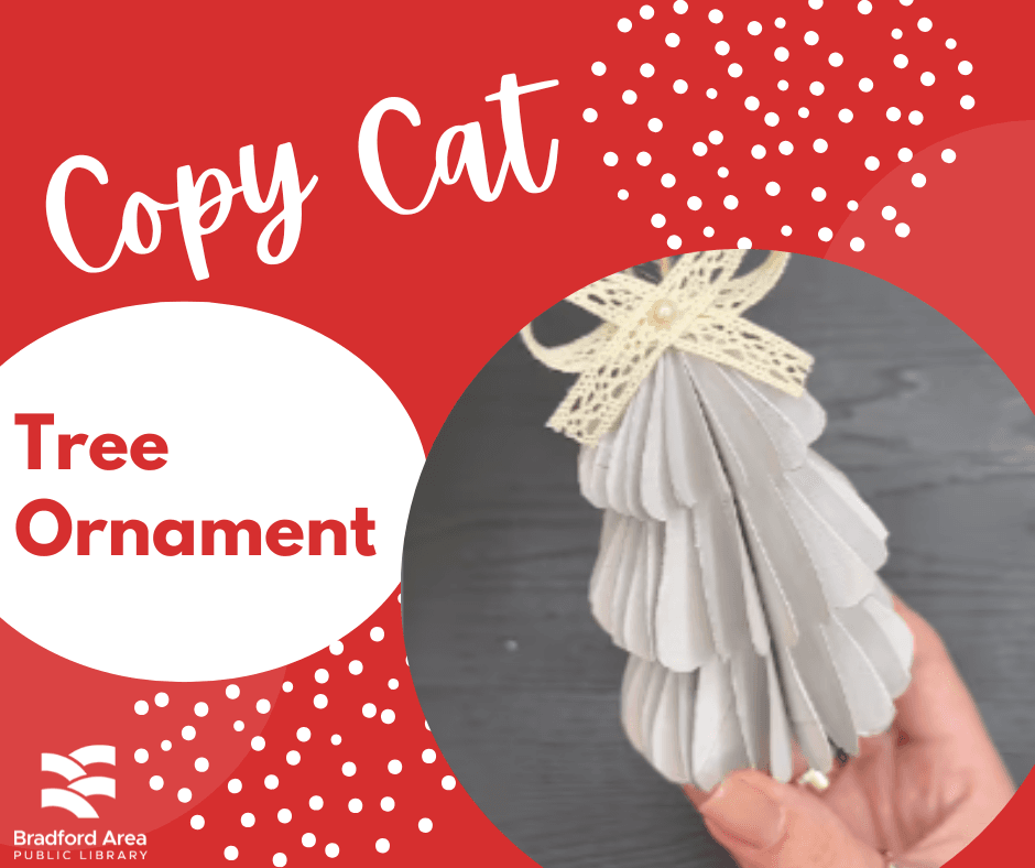 A hand holding a cardboard tree ornament with a bow on top.