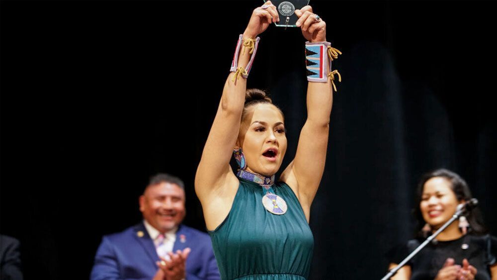 Woman on stage holding up a glass award, with applauding and smiling people in the background.