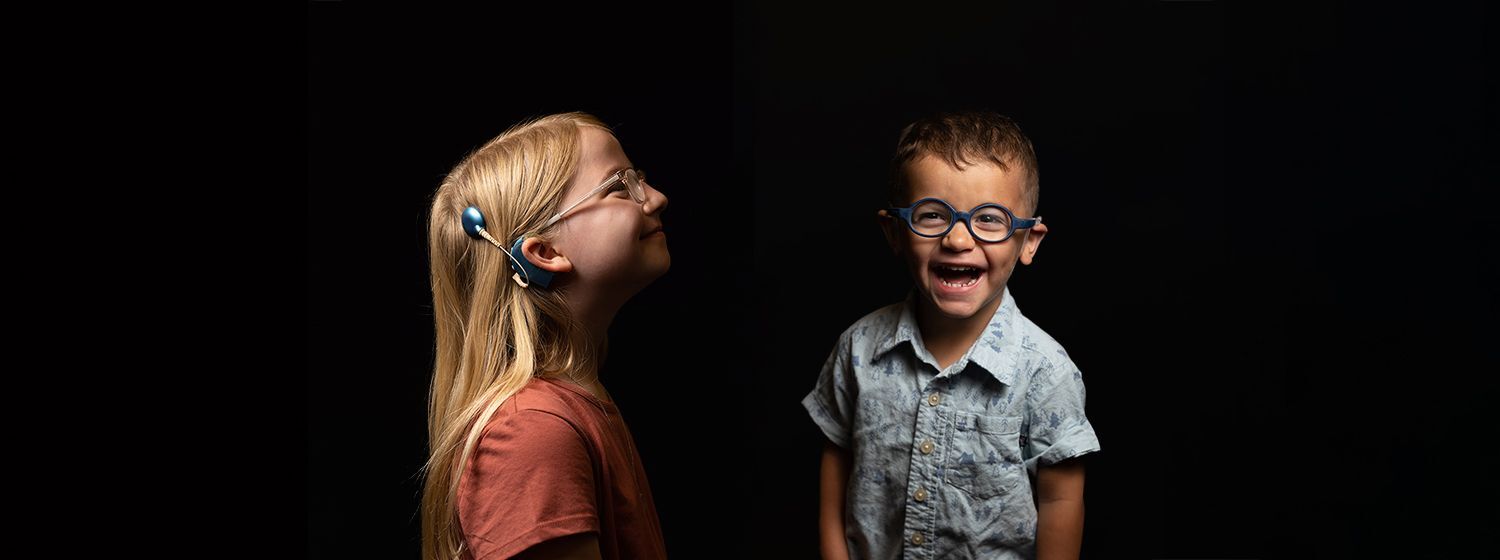 a young girl is standing sideways with her implant on and her glasses another picture she is holding her implant in her hands and smiling at the camera with her glasses on.