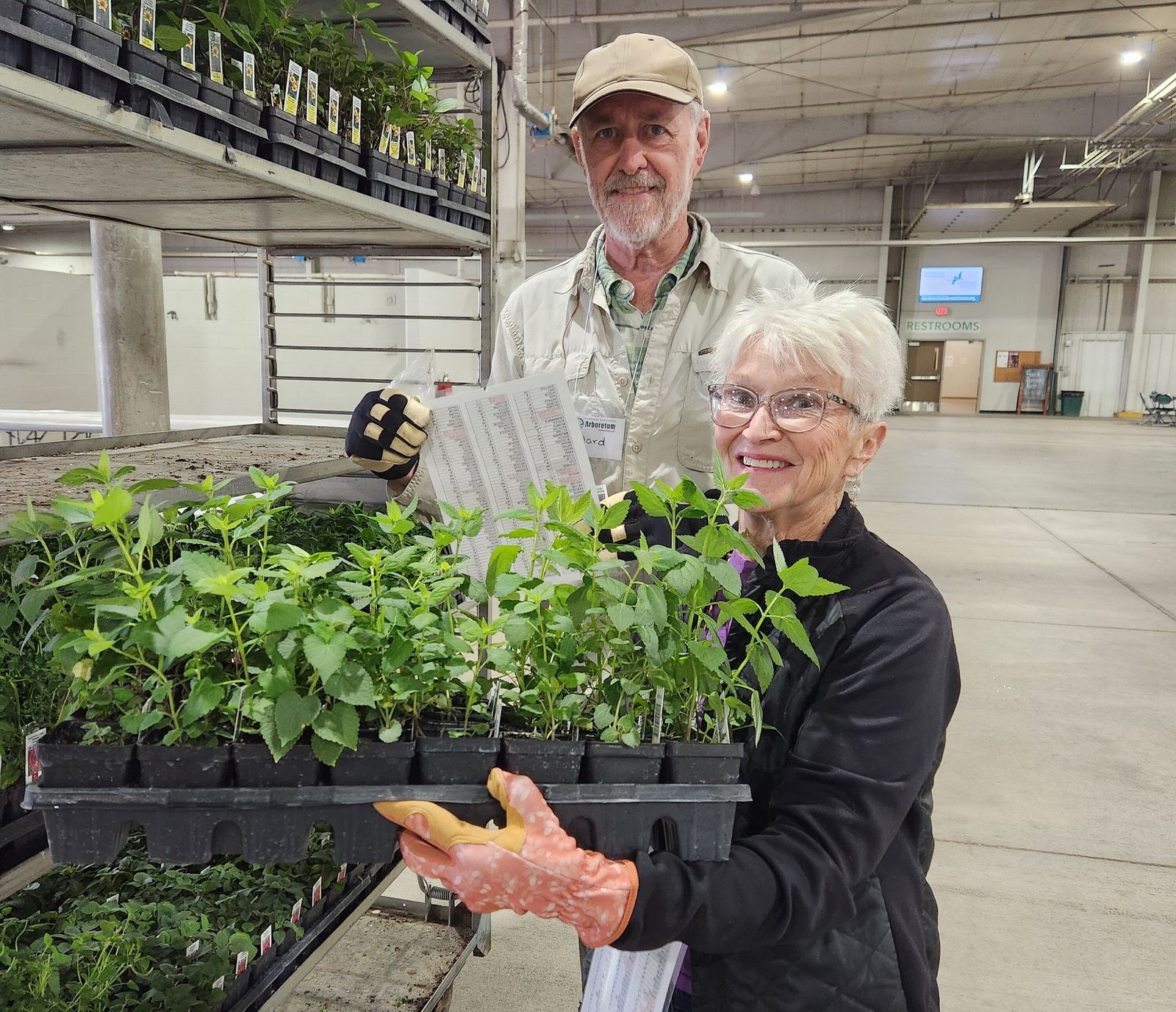A man and a woman hold at large flat of plants at Spring Affair.