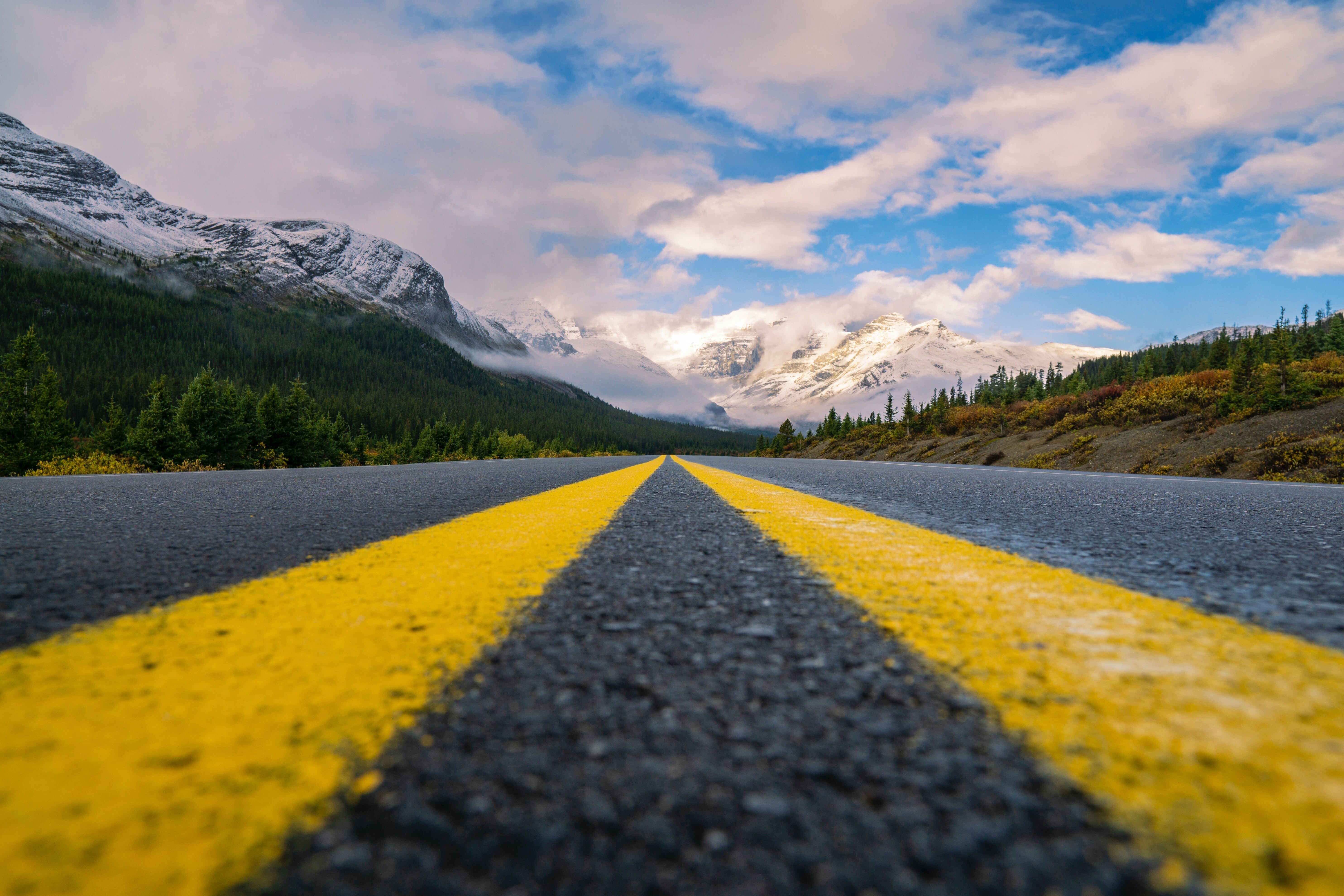 Two yellow lines on a highway converge toward distant mountains and the horizon