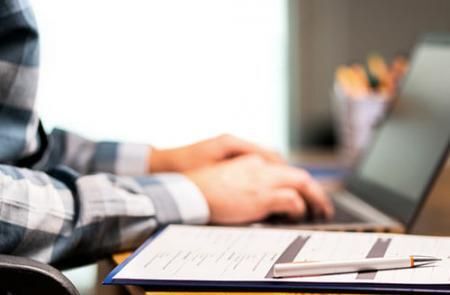 Hands are resting on a keyboard with paperwork and a pen next to it