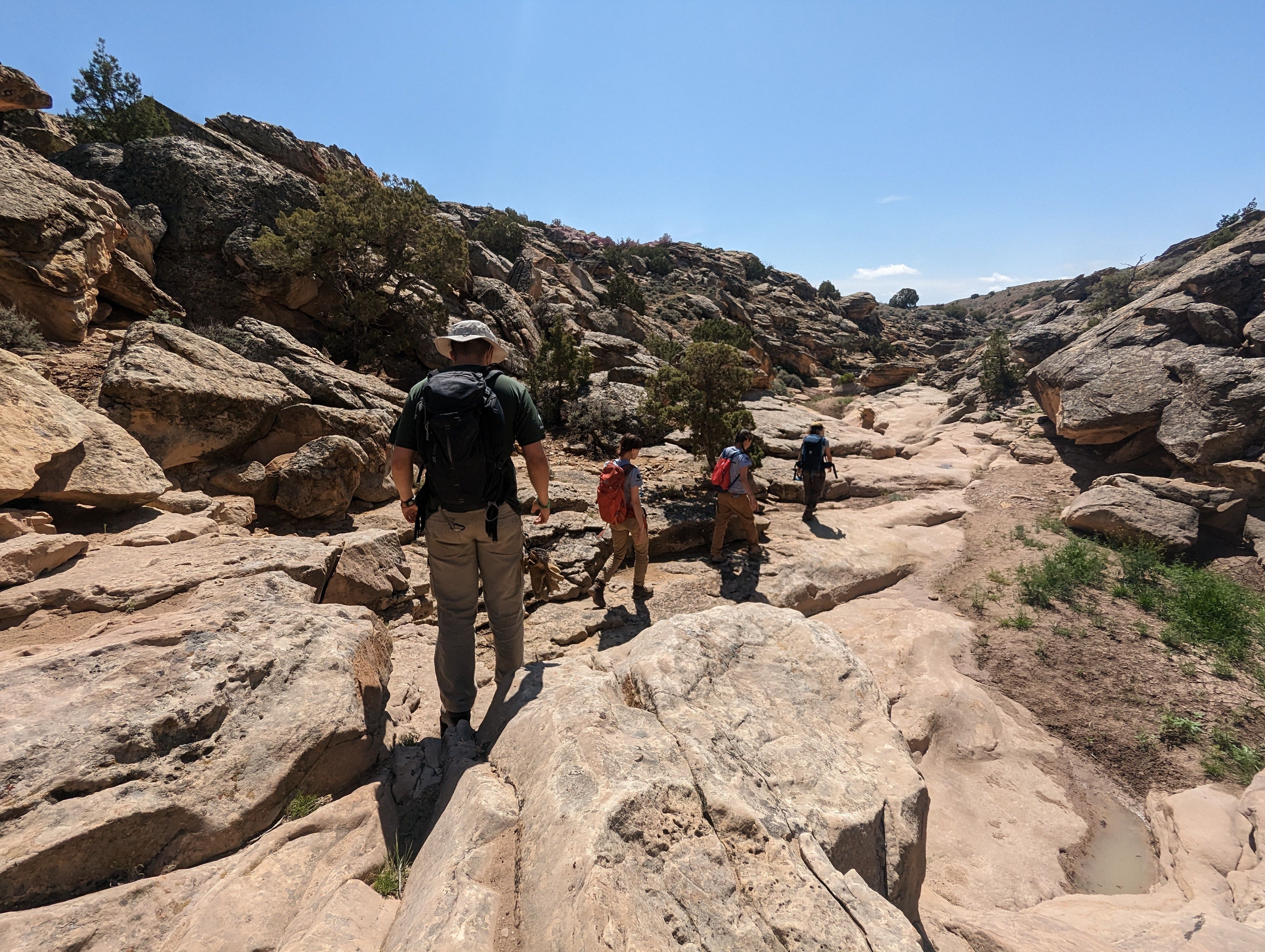 A crew walks on stone in the desert, away from the camera.