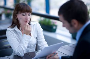 business woman in white shirt reading paper sitting across from business man in suit