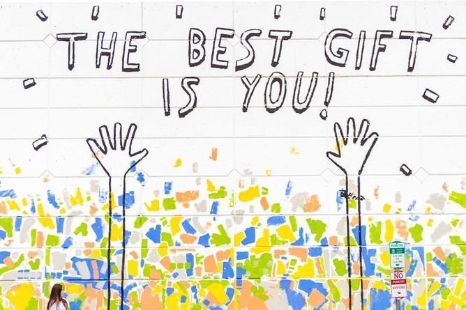 Mural on a brick wall featuring hands, confetti, and the slogan, "The best gift is you!"