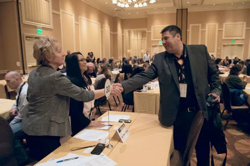 Conference room with people at tables, a man and woman shaking hands in the foreground.