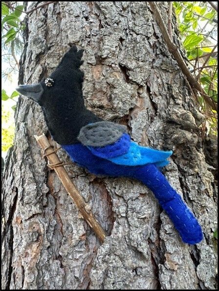 A blue jay-like bird with a black mohawk, made out of felt and stitched together. Displayed as if it is perched on a tree