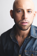 Anthony Michael Lopez, a bald man with a dark blue button up shirt. He is facing the camera directly and has a serious look on his face, with some facial hair. The background is light.