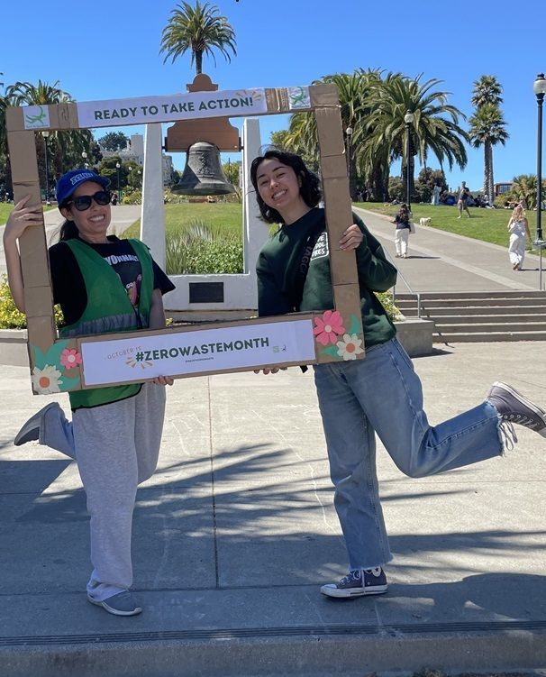 1 Race to Zero Waste and 1 Love Dolores staff pose at Dolores Park with the #ZeroWasteMonth frame, which says "Ready to take action!" at the top.