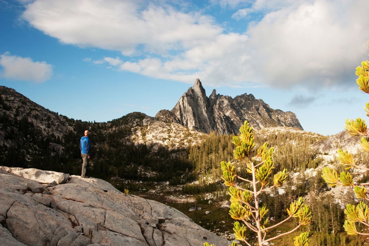 A picture of a male standing on a rock looking at Prusik Peak in the Enchantments.