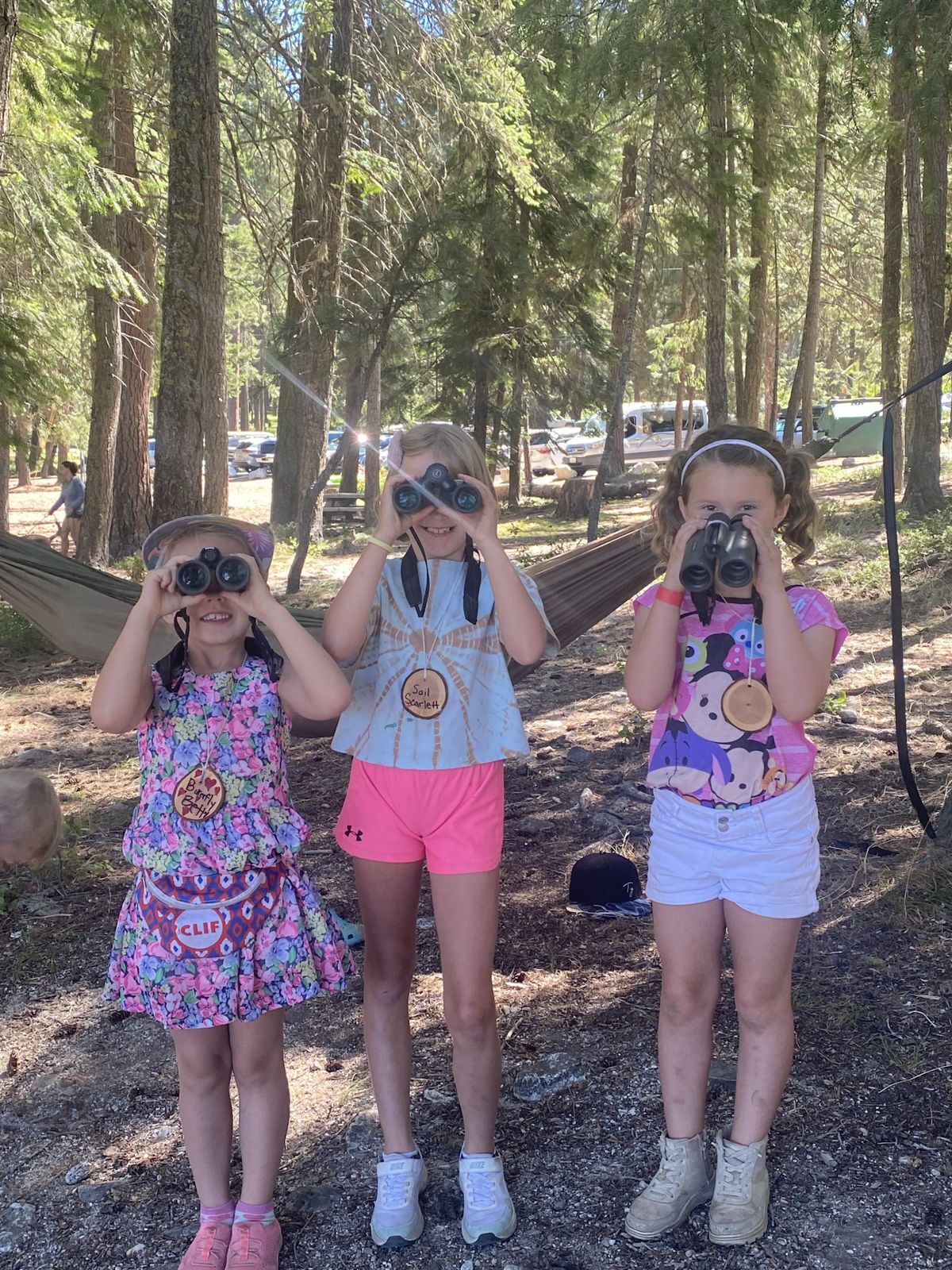 Three young girls aiming their binoculars at the camera at Lake Wenatchee State Park.