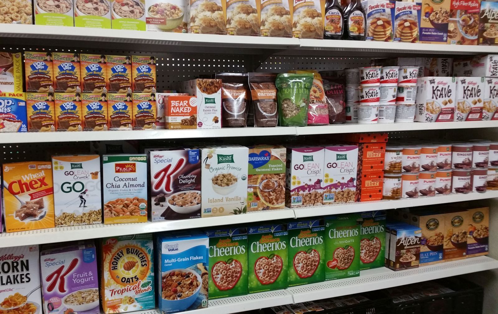 Root Cellar pantry shelf at CARE Community Center displaying a variety of breakfast items including Cheerios, Special K, Pop-Tarts, Kashi cereals, pancake mix, and granola—highlighting available food assistance options