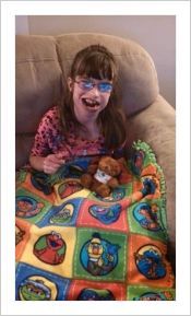 Young girl sitting on the sofa, smiling at the camera, with a colorful quilt on her lap